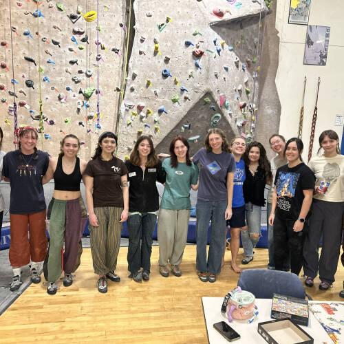 a dozen attendees of the monthly women on the wall program posing for a photo in front of the wall